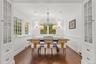 Bright breakfast nook surrounded by windows that fill the space with natural light and peaceful garden views. Classic white wainscoting, warm hardwood