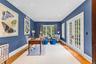 Elegant home office featuring rich blue walls, recessed lighting, and beautiful hardwood floors. French doors and large windows provide abundant natur