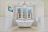 The primary suite offers a serene sanctuary centered around a classic clawfoot soaking tub framed by elegant wainscoting and a sprawling triple-window