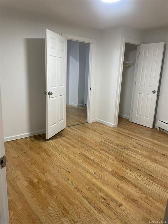 Unfurnished bedroom with light wood-style flooring, a closet, and a baseboard heating unit
