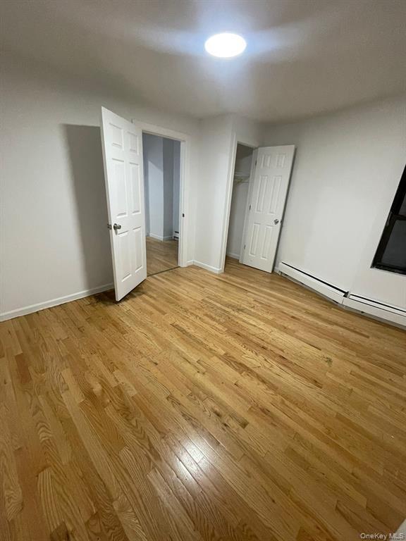 Unfurnished bedroom with a baseboard heating unit, light wood-style floors, and a closet