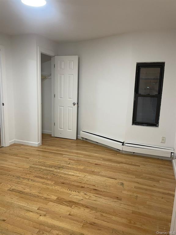 Unfurnished bedroom with a baseboard radiator, light wood finished floors, and a spacious closet