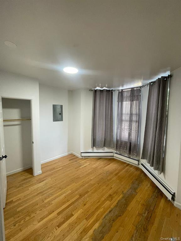 Unfurnished bedroom featuring light wood-style floors, a closet, electric panel, and a baseboard heating unit