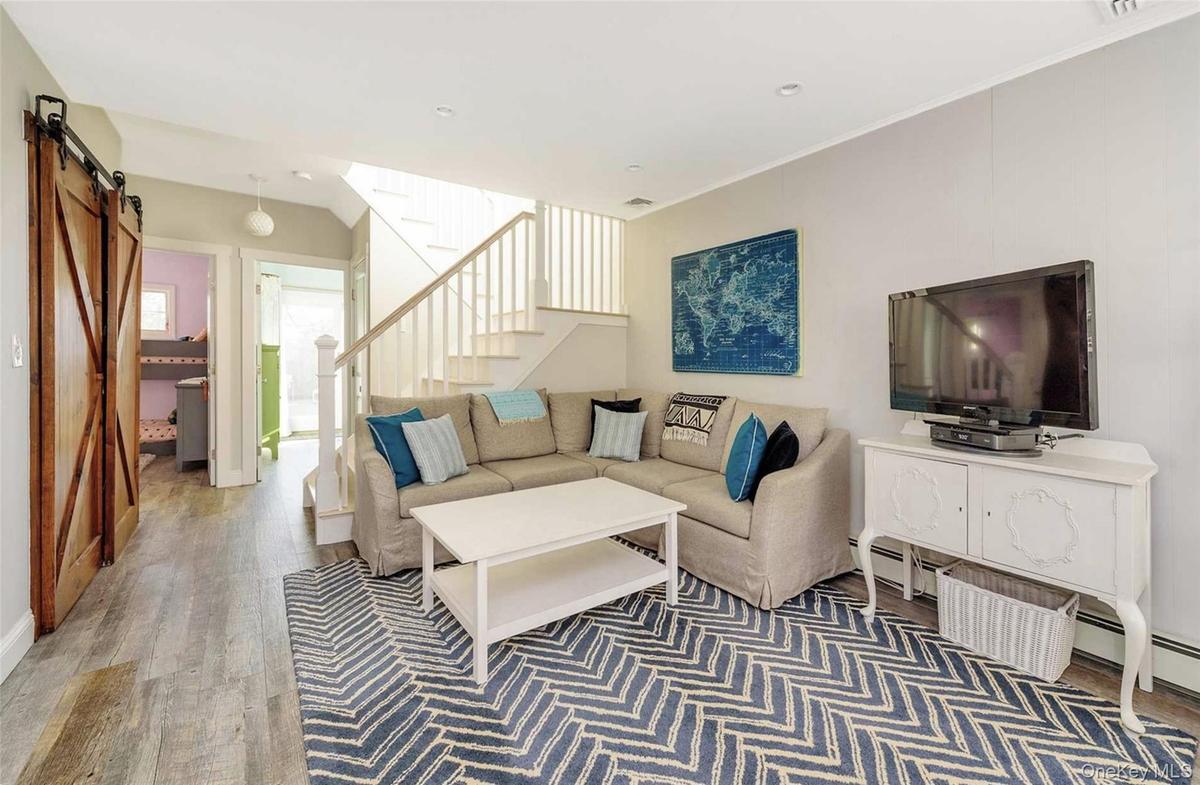 Living room featuring wood-type flooring, a barn door, baseboard heating, and crown molding