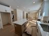 Two tone kitchen featuring light wood-type flooring, a kitchen island, light stone counters, a chandelier, and open floor plan