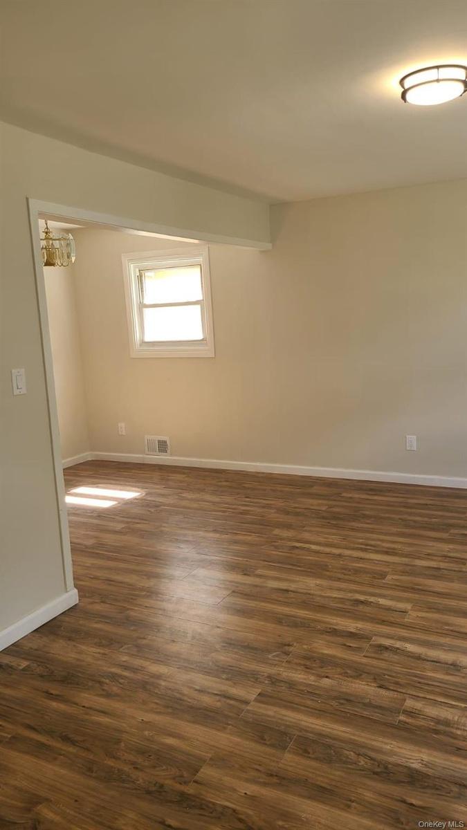 Empty room featuring visible vents, baseboards, and dark wood-style flooring