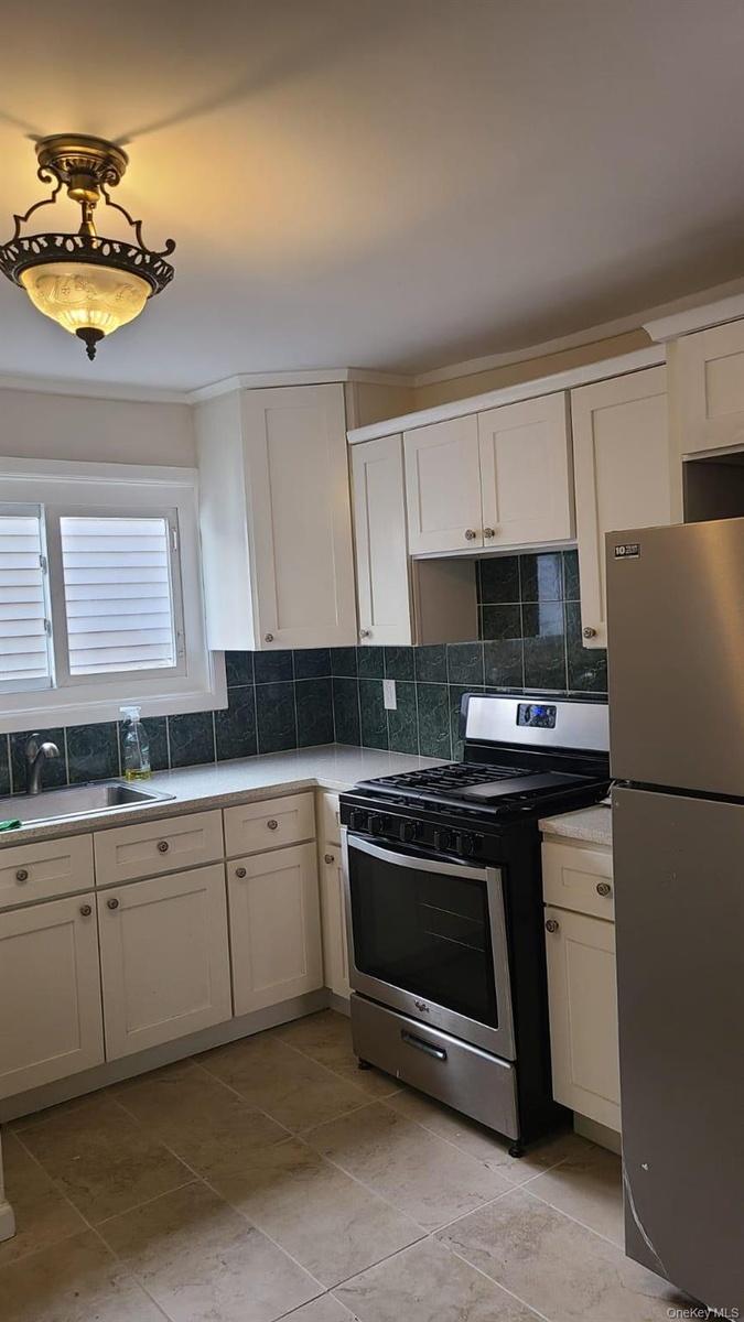 Kitchen featuring a sink, tasteful backsplash, white cabinetry, stainless steel appliances, and light countertops