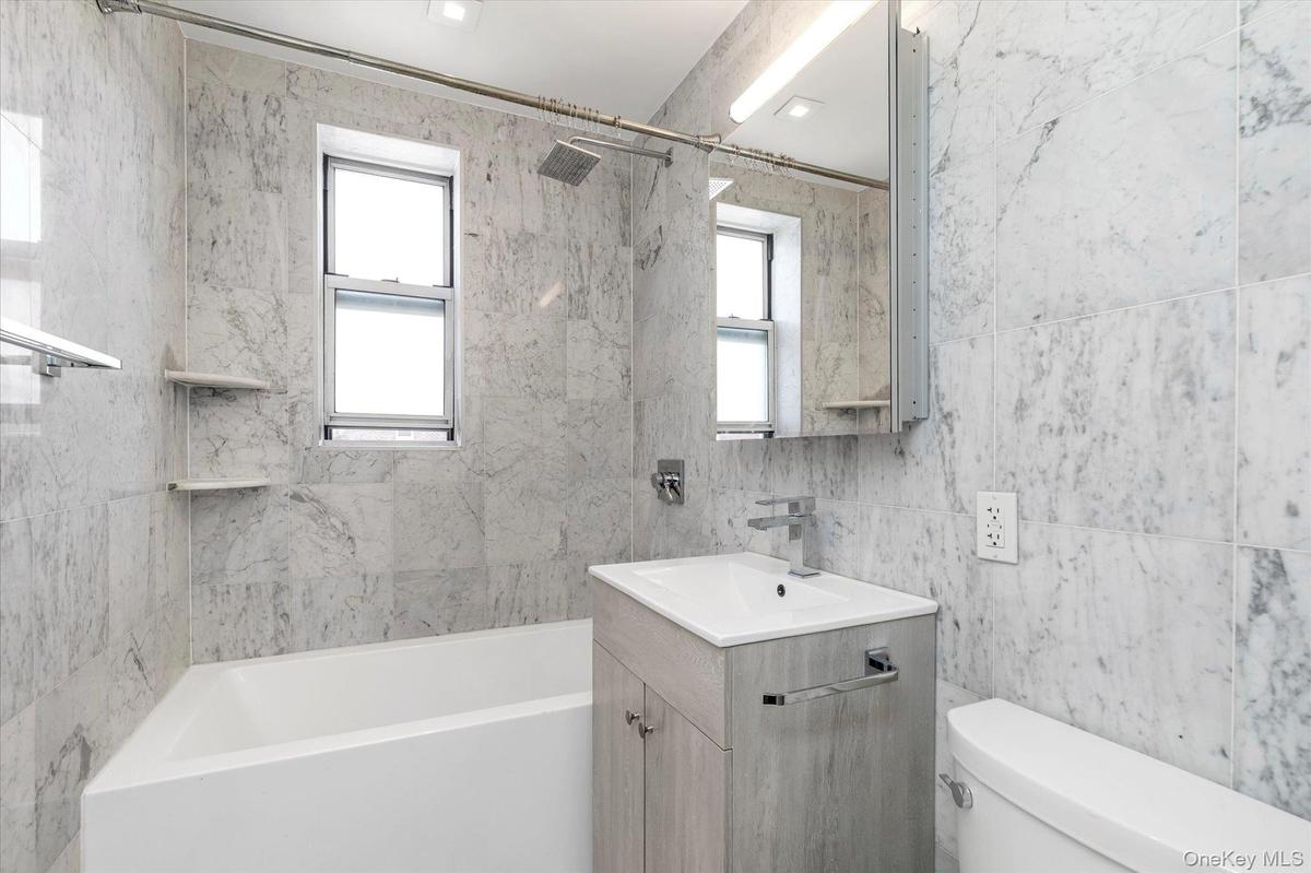 Bathroom featuring vanity, shower / bathtub combination, tile walls, and plenty of natural light
