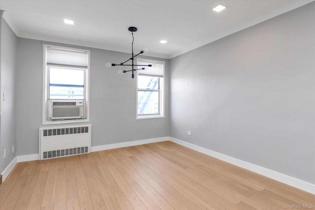 Unfurnished dining area with radiator, light wood-style flooring, hanging lights, cooling unit and recessed lighting