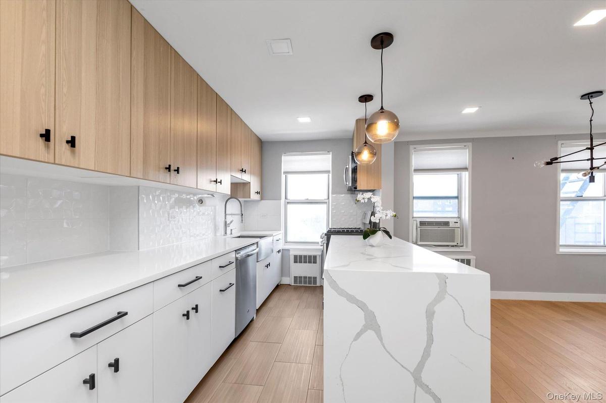 Kitchen featuring backsplash, light stone countertops, light wood-style flooring, stainless steel dishwasher, radiator heating unit, recessed lighting