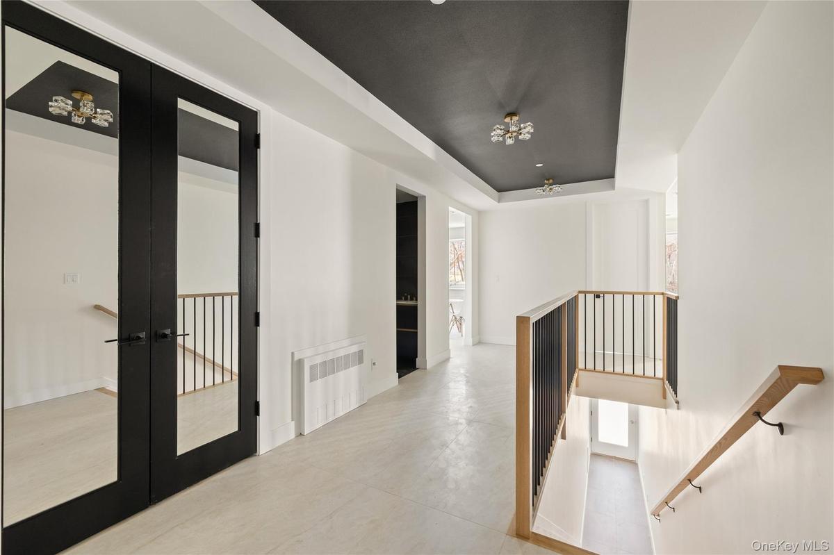 Hallway featuring a tray ceiling, french doors, radiator heating unit, and an upstairs landing