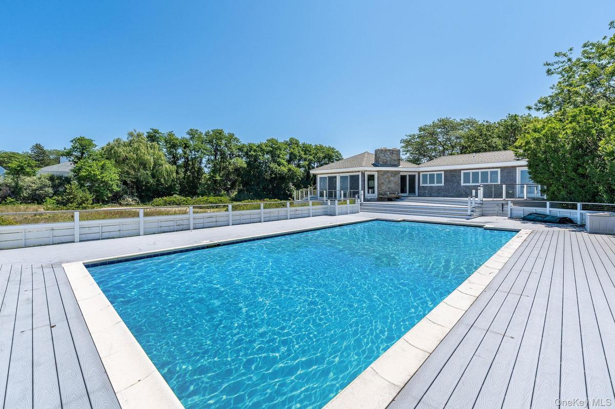 View of swimming pool with a patio area, a deck, and view of scattered trees. gunite pool