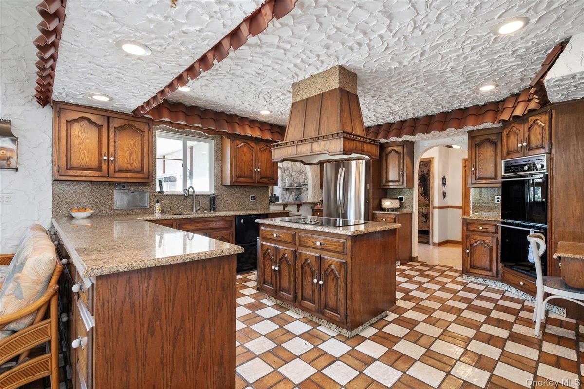 Kitchen with black appliances, a sink, arched walkways, tasteful backsplash, and a peninsula