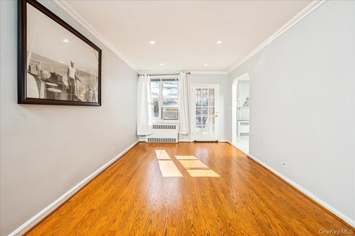 Living room with arched walkways, crown molding, light wood-type flooring, radiator, and recessed lighting