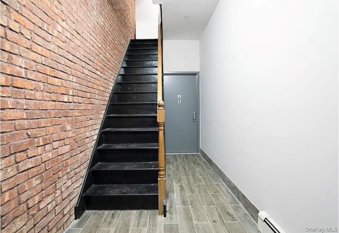 Stairs featuring wood tiled floors, brick wall, and baseboard heating