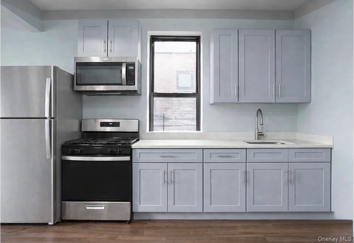 Kitchen with stainless steel appliances, light stone countertops, gray cabinetry, and dark wood-style flooring