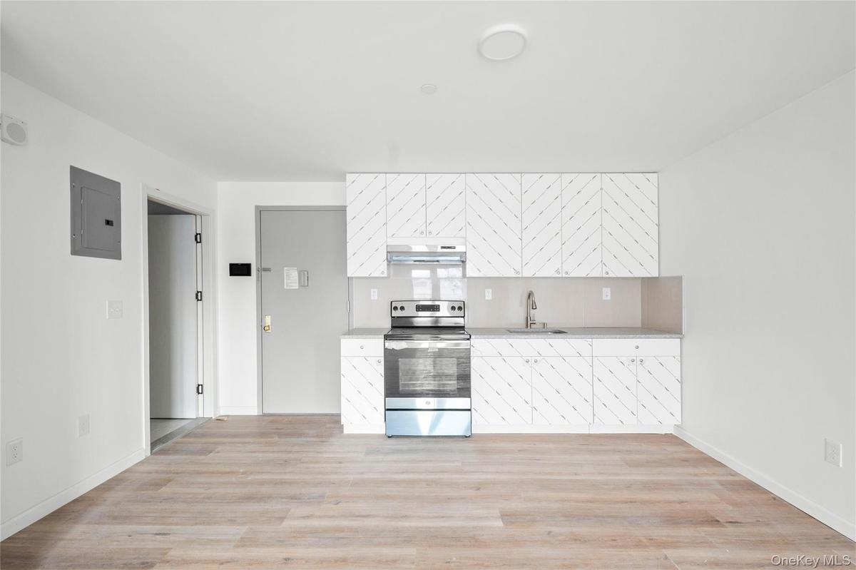 Kitchen featuring stainless steel electric range oven, electric panel, white cabinetry, light wood-type flooring, and tasteful backsplash
