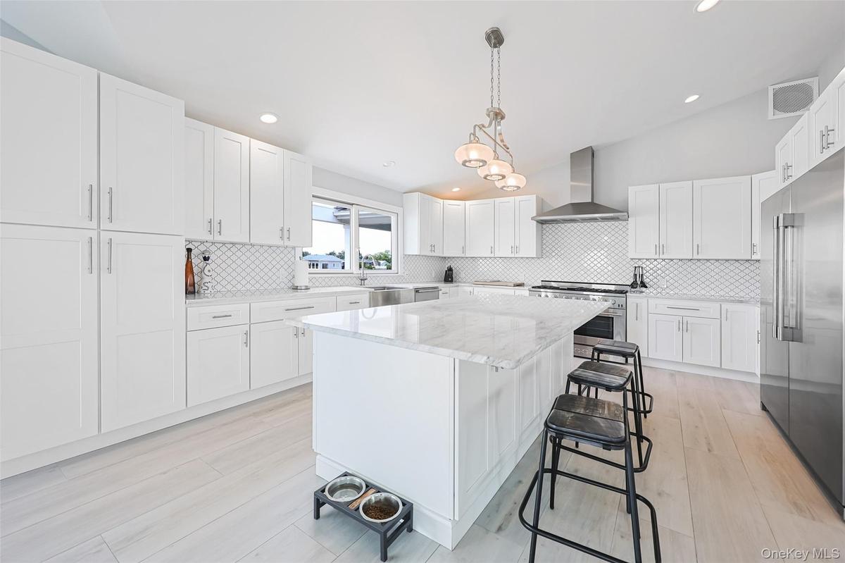Kitchen featuring wall chimney range hood, premium appliances, a kitchen island, a breakfast bar area, and backsplash