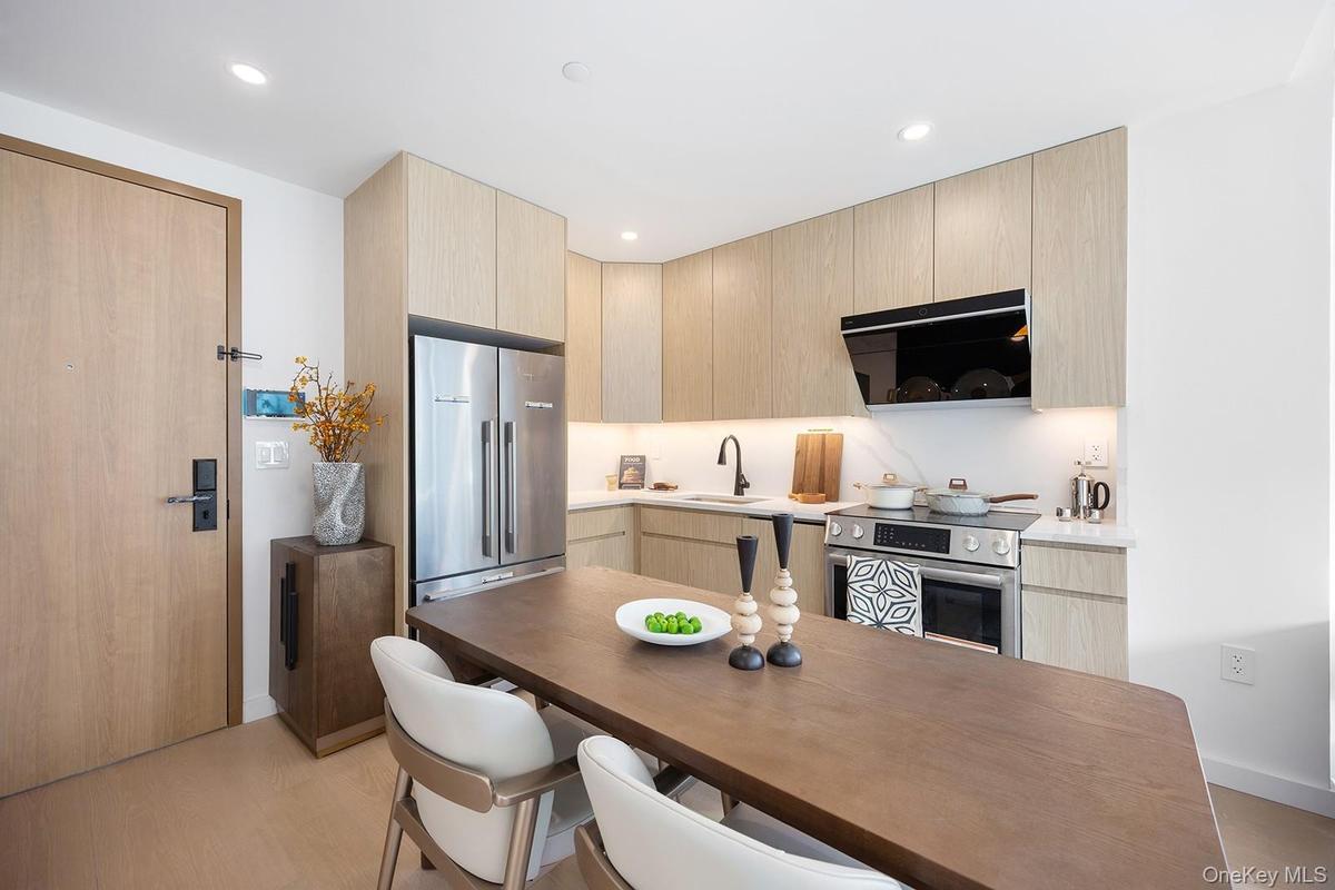 Kitchen with light brown cabinetry, modern cabinets, stainless steel appliances, light wood-type flooring, and ventilation hood