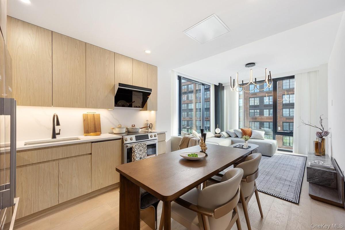 Kitchen with light brown cabinetry, expansive windows, modern cabinets, appliances with stainless steel finishes, and range hood