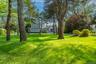 Expansive lawn with mature trees, established landscaping, and a paved driveway leading to the residence