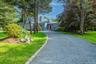 Long gravel driveway with granite block edging, leading to a contemporary residence with a red front door, surrounded by mature trees and manicured la