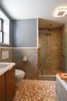 Full bath with a stall shower, vanity, wainscoting, and tile walls. Heated spa-like floors and large bathtub add to spa-like space.
