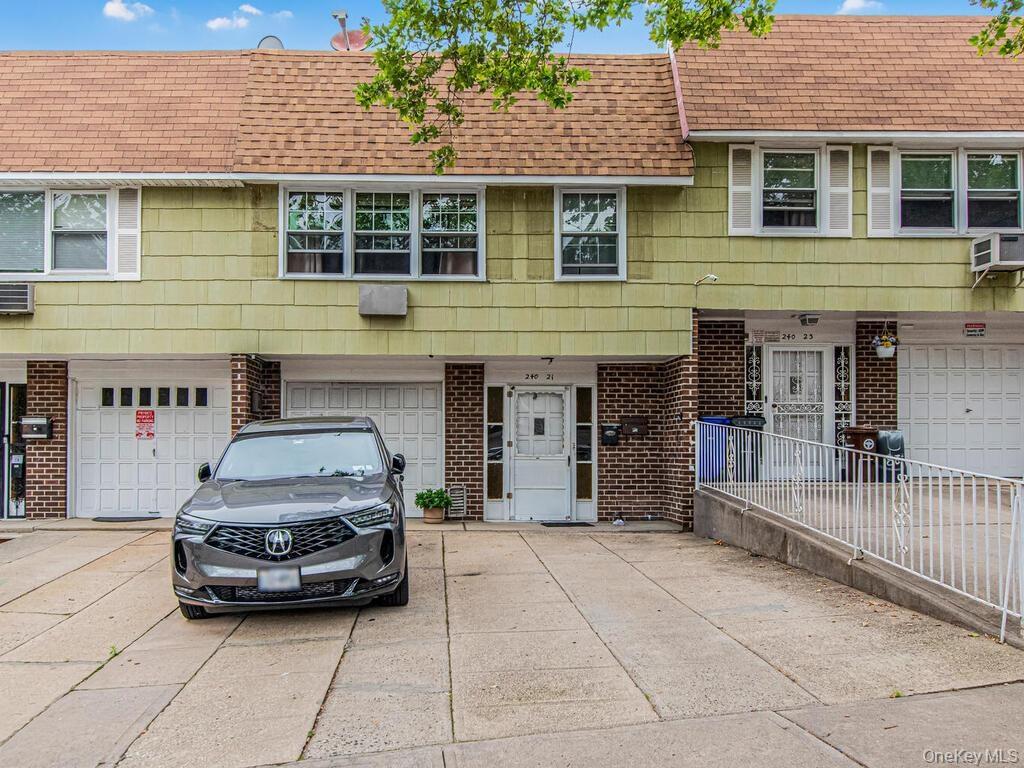 Townhome / multi-family property with a shingled roof, brick siding, driveway, and an attached garage