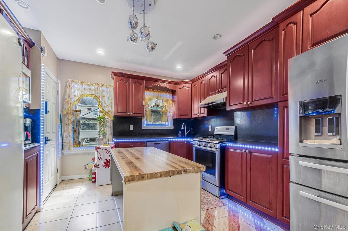 Kitchen featuring reddish brown cabinets, stainless steel appliances, wooden counters, light tile patterned floors, and recessed lighting