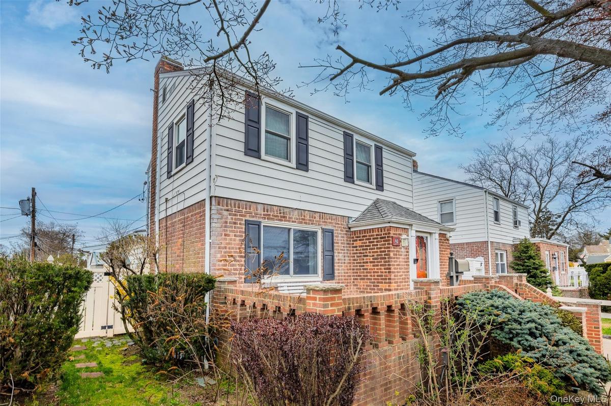 The property features a brick and siding exterior with dark shutters, a front porch with a covered entry, and a fenced yard with established plantings