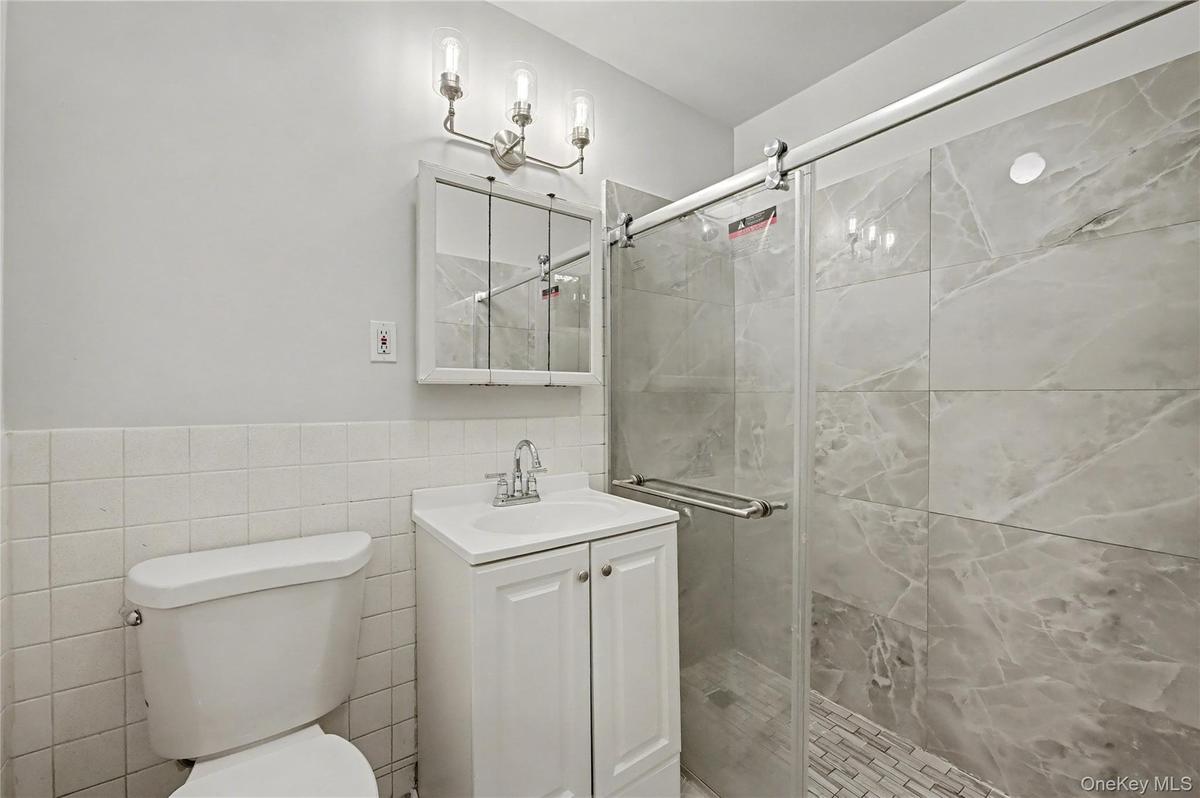 Full bathroom featuring a shower stall, vanity, tile walls, and wainscoting