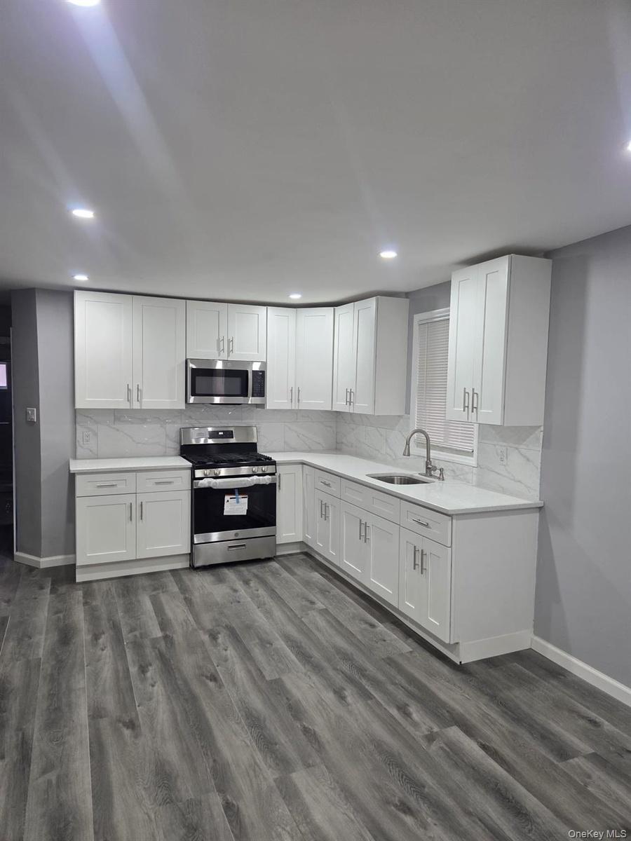 First Floor Kitchen with stainless steel appliances, white cabinetry, backsplash, dark wood-style flooring, and light stone countertops