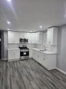 First Floor Kitchen with stainless steel appliances, white cabinetry, backsplash, dark wood-style flooring, and light stone countertops