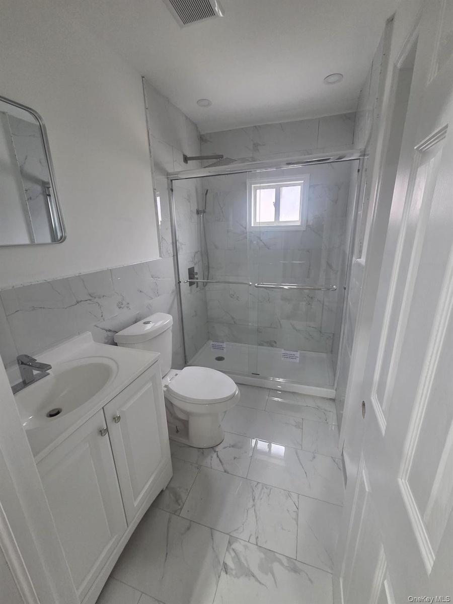 First Floor Bathroom featuring vanity, a tile finish shower, light tile finish flooring, and tile walls