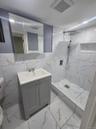 Basement Bathroom featuring a tile finish shower, vanity, tile walls, and light tile finish flooring
