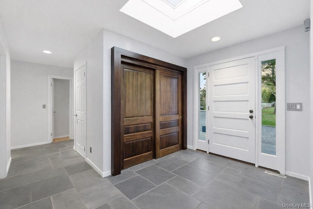 Entryway featuring a skylight, slate tile flooring, a solid white panel door with sidelights, and recessed lighting