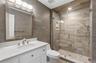 White vanity with a light-toned countertop, framed mirror, and a glass-enclosed shower featuring a handheld showerhead