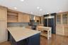 Spacious kitchen featuring wood-finish flooring, light wood cabinetry with glass-front uppers, a dark island with a light-toned countertop, and a buil
