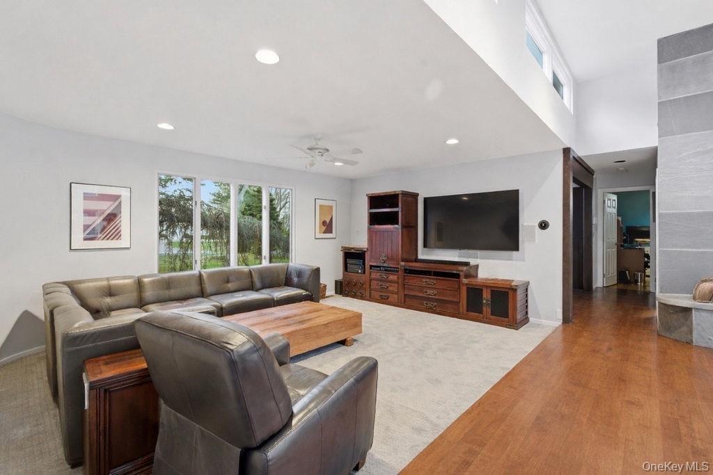 Expansive living area with recessed lighting, large windows, wood-finish flooring, and a stone-clad architectural feature