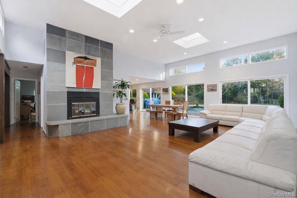 Vaulted ceilings, wood-finish flooring, stone-clad fireplace with hearth, multiple skylights, and expansive sliding glass doors