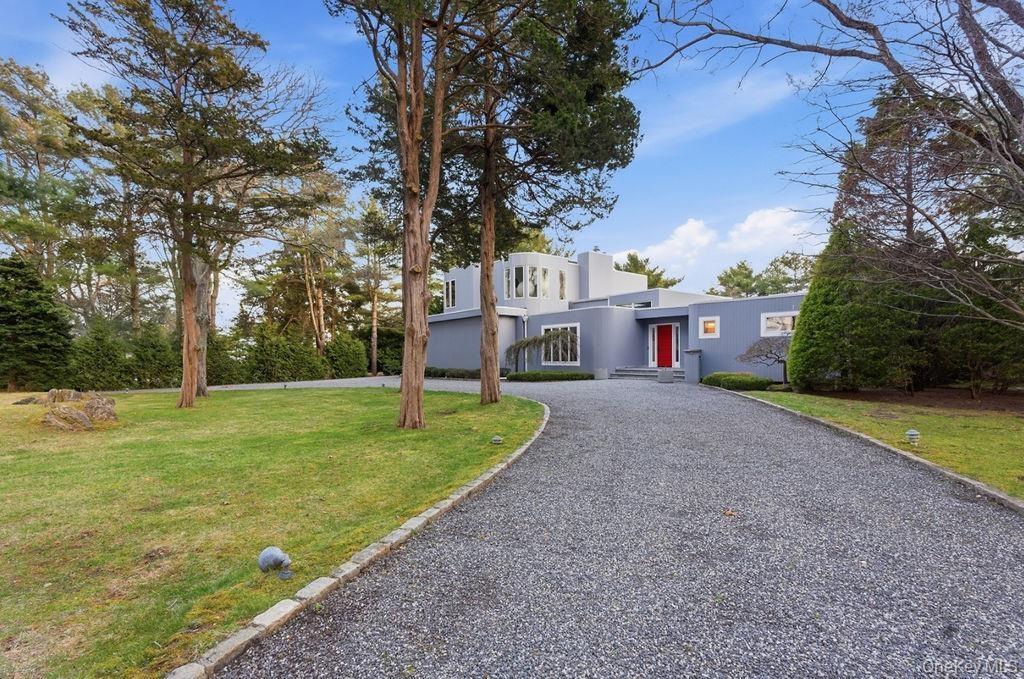 Modern exterior with a circular drive, mature trees, and a manicured lawn