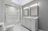Dual vanity with integrated sinks and brushed nickel fixtures, under-mount bathtub with sliding glass enclosure, white tile tub surround, and a skylig