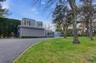 Contemporary architecture with curved walls and multiple windows, gravel driveway, and expansive lawn with mature trees