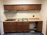 Kitchen featuring light countertops, under cabinet range hood, stainless steel gas stovetop, brown cabinetry, and dark stone finish flooring