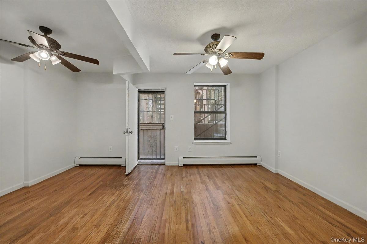 Spare room featuring a ceiling fan, a baseboard heating unit, and light wood-type flooring