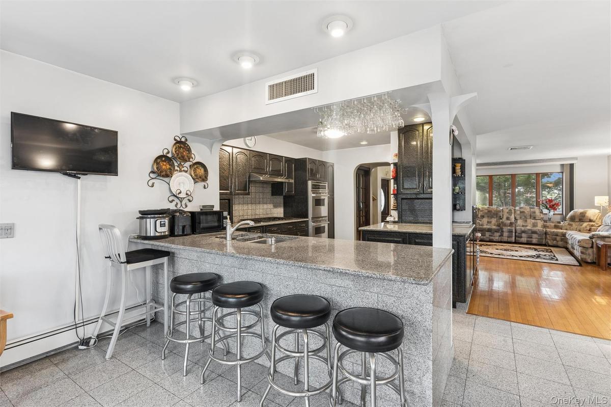 Kitchen featuring a kitchen bar, arched walkways, a peninsula, a baseboard radiator, and light stone counters