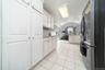 Kitchen with freestanding refrigerator, white cabinetry, light stone countertops, light tile patterned floors, and a kitchen island with sink