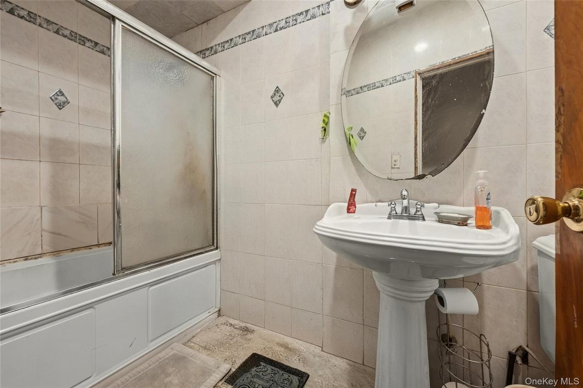 Bathroom featuring bath / shower combo with glass door and tile walls