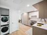 Kitchen featuring stainless steel appliances, a sink, stacked washer / drying machine, light countertops, and white cabinets