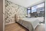 Bedroom featuring wallpapered walls, baseboards, wood finished floors, an accent wall, and a wall of windows